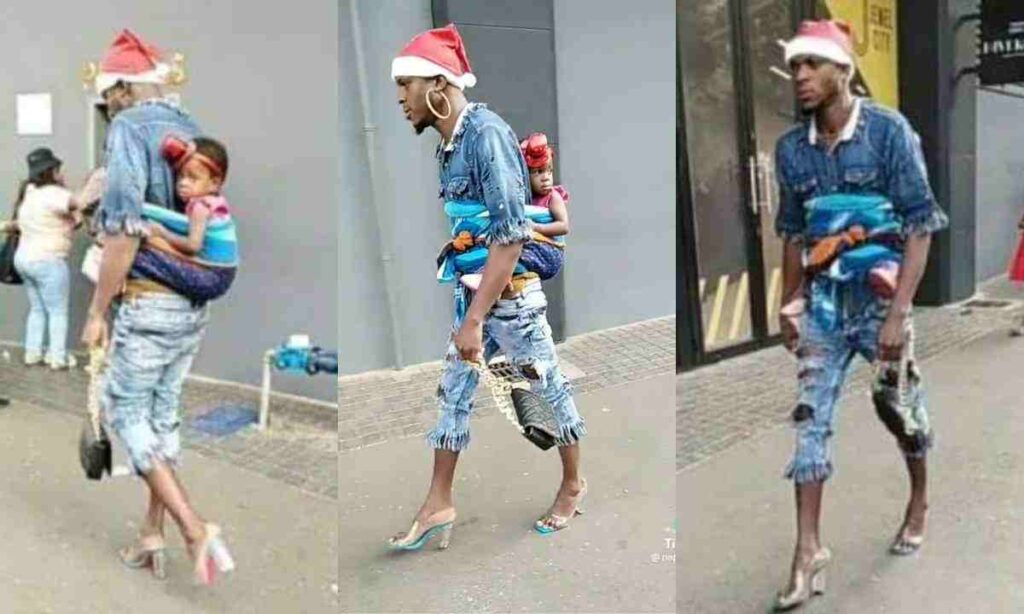 “What a woman can do, A man can do better” – Man in High Heels and Earrings Appears in Streets With Baby on His Back in Funny Video (Watch)